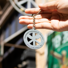 Load image into Gallery viewer, Hand holding a keychain with a peace symbol design outdoors
